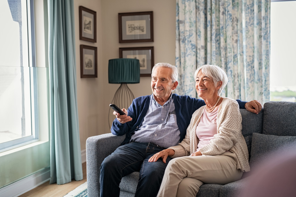 Seniors watch TV for entertainment while man using remote control.